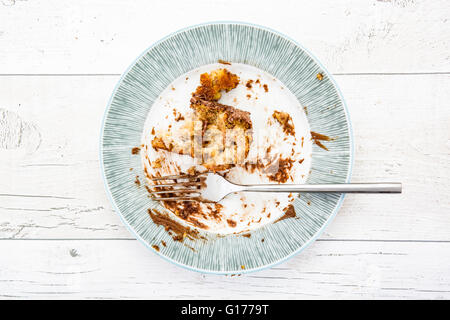 Scatto dall'alto di una piastra a vuoto con gli avanzi di un pasto su un bianco sullo sfondo di legno Foto Stock