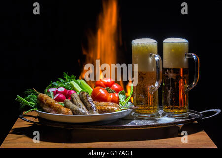 Due birre e salsicce con fiamma su sfondo Foto Stock