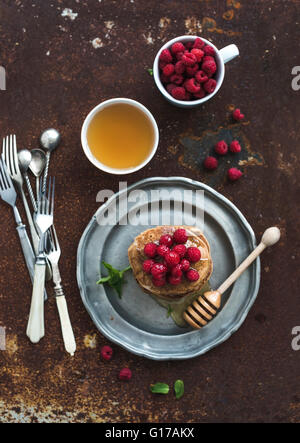 Set colazione. Frittelle di farina di grano saraceno con lamponi freschi, miele e foglie di menta su grunge sfondo metallico, vista dall'alto, selectiv Foto Stock