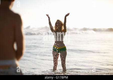 Donna in ocean indossando un bikini bracci sollevati spruzzi Foto Stock