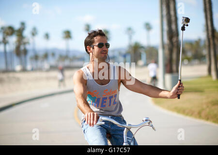 Ciclista maschio facendo ciclismo selfie presso la spiaggia di Venezia, Los Angeles, California, Stati Uniti d'America Foto Stock