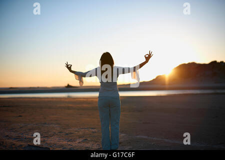 Vista posteriore della donna con le braccia aperte sul Cannon Beach al tramonto, CALIFORNIA, STATI UNITI D'AMERICA Foto Stock