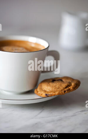 Burro di arachidi e biscotti al cioccolato e una tazza di caffè su un marmo bianco tabella Foto Stock