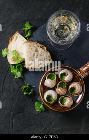 Escargots de Bourgogne - Lumache con burro alle erbe, piatto gourmet, nella tradizionale coppa in ceramica con prezzemolo, pane e bicchiere di whi Foto Stock