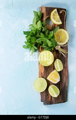 Fettine di lime e limoni con mazzetto di menta fresca sul tagliere di legno sulla luce blu sullo sfondo a trama. Vista dall'alto. Con copia Foto Stock