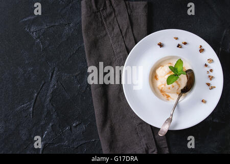 Bianco piastra in ceramica con caramello e burro noisette gelato, serviti con sciroppo di caramello, cucchiaino, menta e croccante di dadi sulla gr Foto Stock