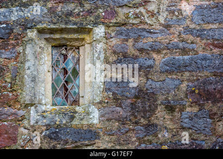 Una vecchia chiesa in pietra con finestre in vetro colorato e condurre il lavoro nel villaggio di Cockington Chiesa, Torquay, Devon, Regno Unito Foto Stock