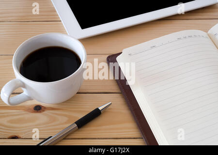 Office Workplace con schermo vuoto tablet, penna, un notebook e una tazza di caffè sul vecchio tavolo in legno.Close up Foto Stock