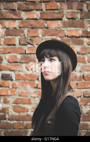 Giovane donna di fronte a un muro di mattoni Foto Stock