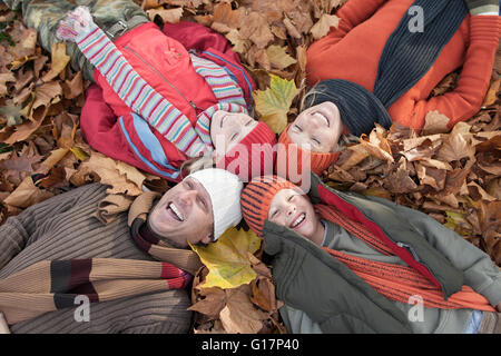 Famiglia giacente insieme in foglie di autunno, ridendo Foto Stock