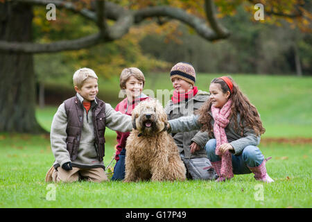 Quattro bambini nel parco, accovacciato, accarezzare cane Foto Stock