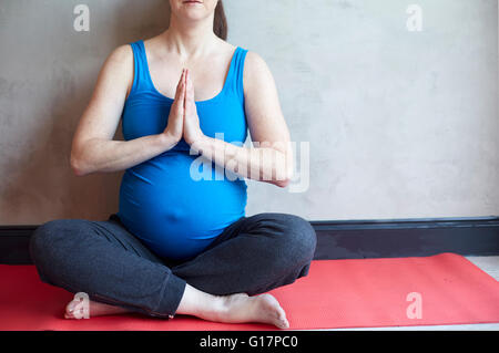 Donna incinta seduta croce gambe, mani insieme nella posa di yoga Foto Stock