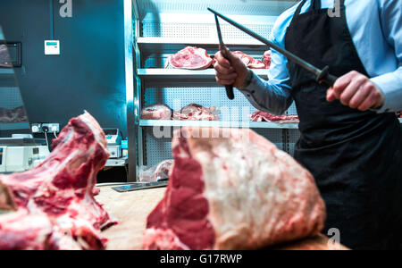 Macellaio coltello affilatura sulla lama di acciaio in macelleria, metà sezione Foto Stock