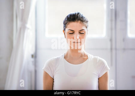 Giovane donna meditando con gli occhi chiusi in appartamento Foto Stock