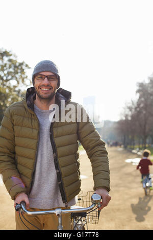 Uomo che indossa knit cappello e occhiali azienda bicicletta guardando sorridente della fotocamera Foto Stock