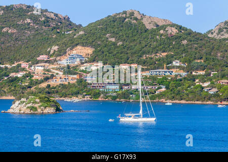Il paesaggio costiero di Porto-Vecchio bay, Corsica, Francia. Bianco yacht a vela andare vicino alla piccola isola rocciosa Foto Stock