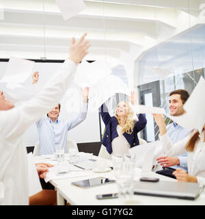 La gente di affari celebra il loro successo e genera fogli di carta in aria durante una riunione di affari Foto Stock