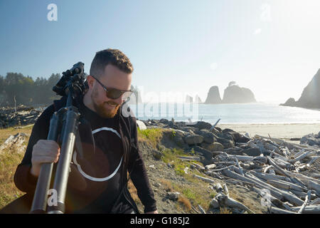 Fotografo maschio che trasportano treppiede sulla costa, Puget Sound, nello Stato di Washington, USA Foto Stock