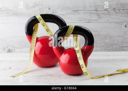 Due kettlebells rosso con nastro di misurazione sul bianco rustico tavolo in legno. Salute e fitness concetto. Foto Stock