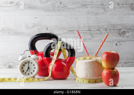 Due kettlebells rosso con nastro di misurazione, bere noce di cocco, cannucce, mele e vintage orologio sul bianco rustico tavolo in legno. Healt Foto Stock