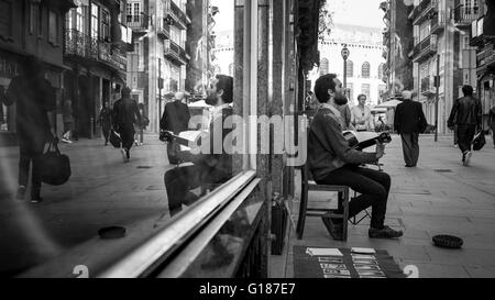 Un maschio di musicista di strada è suonare la chitarra davanti a un negozio di windows, porto, Portogallo. Foto Stock