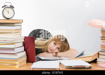 Una studentessa lay dietro una scrivania zeppa di libri e giornali Foto Stock