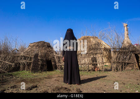 Un oromo etiope donna vestita di nero burqa sorge nella parte anteriore del suo rifugio, Amhara Region, Artuma, Etiopia Foto Stock