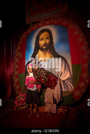 I bambini in Medhane Alem chiesa rupestre di fronte ad un enorme dipinto di Gesù, Amhara Region, Lalibela, Etiopia Foto Stock
