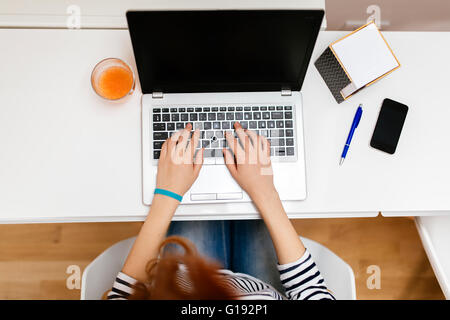 Dai capelli rossi donna che lavorano su computer portatile con la bevanda a portata di mano Foto Stock