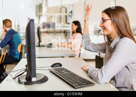 Bellissima fanciulla alzando la mano in aula mentre è seduto alla scrivania Foto Stock