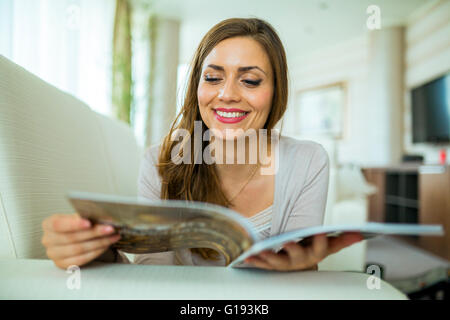 Bella donna su un divano, la lettura di una carta in una ben illuminata ed elegante soggiorno Foto Stock