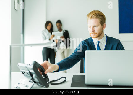 Imprenditore circa per rispondere al telefono con due belle, giovani donne avente una conversazione in background Foto Stock