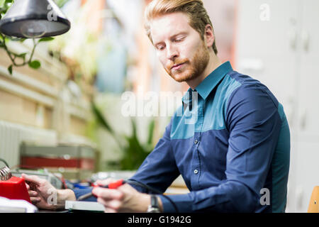 Giovane uomo bello la saldatura di una scheda a circuito stampato e lavorando sulla bulloneria di fissaggio Foto Stock