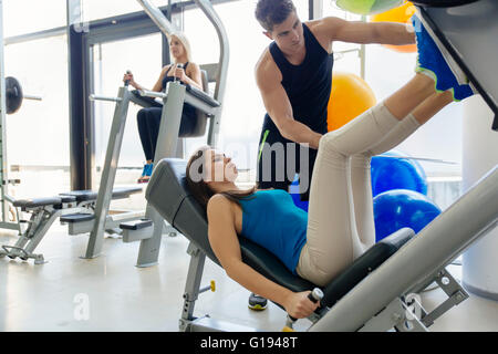 Bella donna gamba facendo esercizi in palestra con l'aiuto di personal trainer Foto Stock