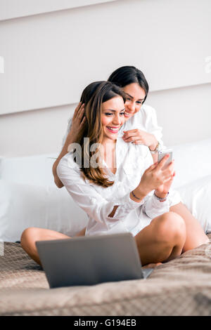 Gorgeous brunettes alla moda in camicie lavorando su un computer portatile mentre nel letto Foto Stock