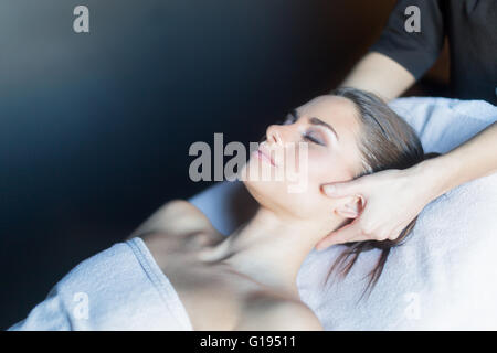 Massaggiatore trattare la faccia di una bella e giovane donna disteso sul lettino da massaggio Foto Stock