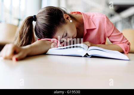 Bella donna graziosa addormentato sul tavolo durante lo studio e la lettura di un libro Foto Stock