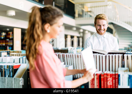 Bella felice gli studenti che studiano e flirtare in una biblioteca moderna Foto Stock