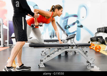 Giovane maschio formatore dando istruzioni ad una donna in una palestra e di essere di supporto Foto Stock