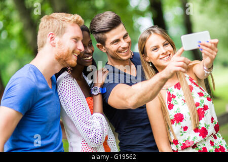 Un gruppo di giovani e coppie tenendo selfies nella natura e sorridente Foto Stock