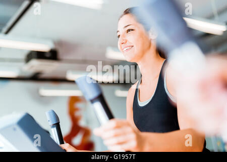 Giovane e bella signora utilizzando il trainer ellittico in una palestra in uno stato d'animo positivo Foto Stock
