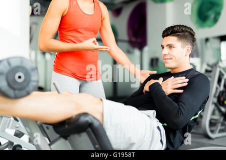 Bella giovane donna istruire un giovane uomo in palestra e si affaccia sul suo allenamento Foto Stock