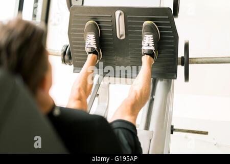 Giovane maschio lavora in una palestra e facendo esercizi di gamba Foto Stock