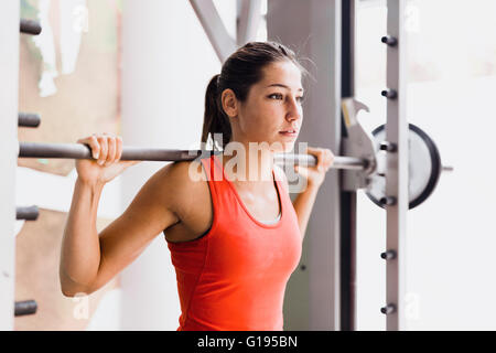 Focalizzato giovane bella donna sollevamento pesi nella palestra Foto Stock
