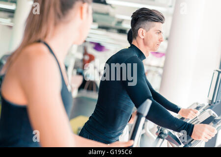 Uomo bello e giovane e bella donna che utilizza un motore passo-passo in una palestra e avere una conversazione Foto Stock