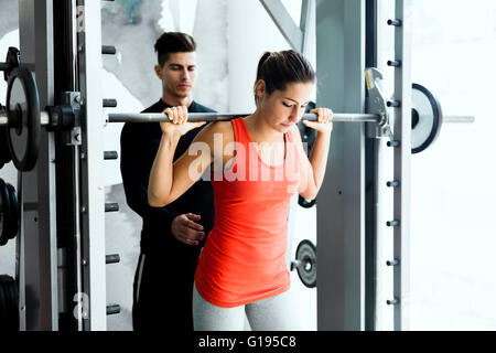 Giovane maschio formatore dando istruzioni ad una donna in una palestra e di essere di supporto Foto Stock