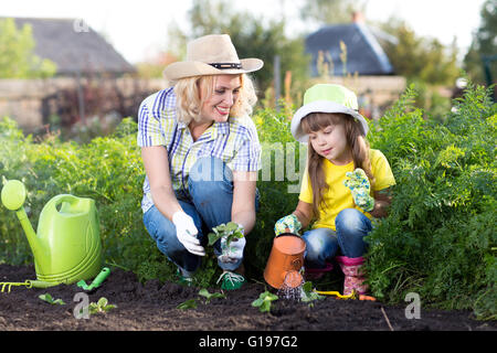 Madre e figlia di capretto piantare piantine di fragole in un giardino. Bambina nuovo di irrigazione delle piante. Foto Stock