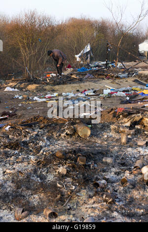 L'uomo alla ricerca di ciò che è rimasto dei suoi beni dopo l'incendio. La Giungla dei profughi migranti & camp, Calais, Francia settentrionale Foto Stock