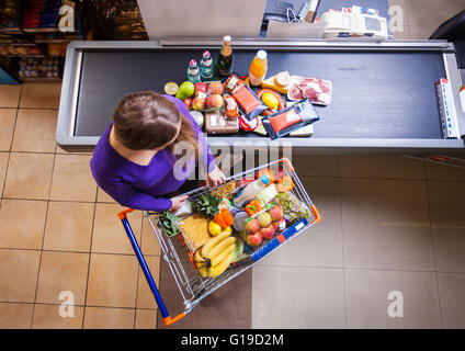 Giovane donna mettendo le merci dal carrello della spesa sul contatore per checkout nel supermercato Foto Stock