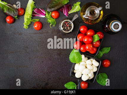 Ingredienti insalata caprese con pomodoro e mozzarella con basilico e erbe oon sfondo nero. Vista superiore Foto Stock